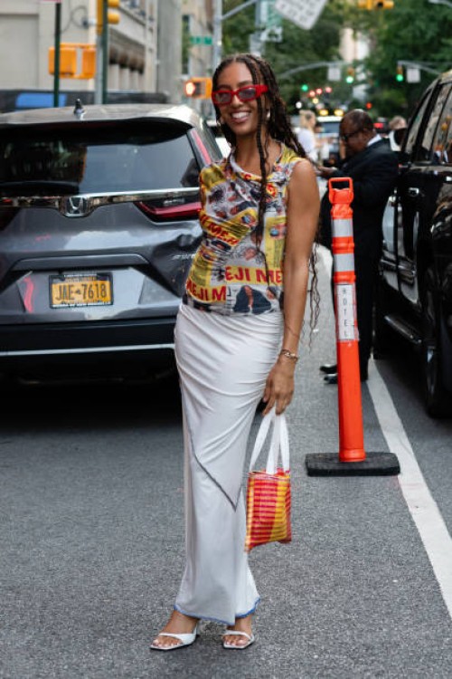 Guest is seen wearing a yellow printed top, white skirt, white shoes, red sunglasses and carrying a red and yellow bag outside the Theophilio show...