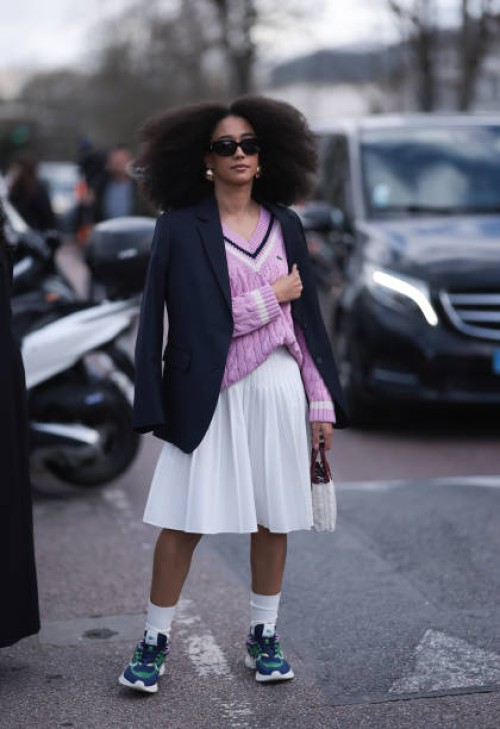 Guest seen wearing a black blazer jacket, purple Lacoste pullover, white skirt, socks, green sneaker, black shades and white bag outside Lacoste Show...
