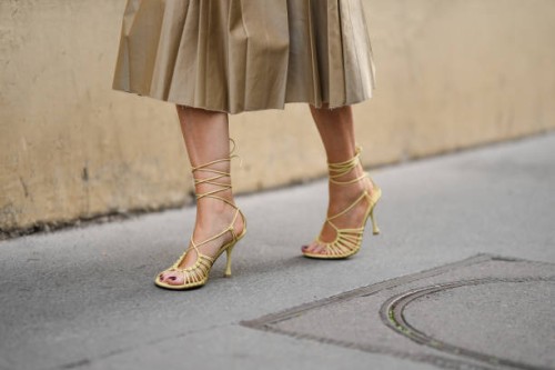 Guest wears a beige pleated / accordion midi skirt from Miu Miu, pale yellow shiny leather strappy heels sandals , outside Victoria Beckham, during...