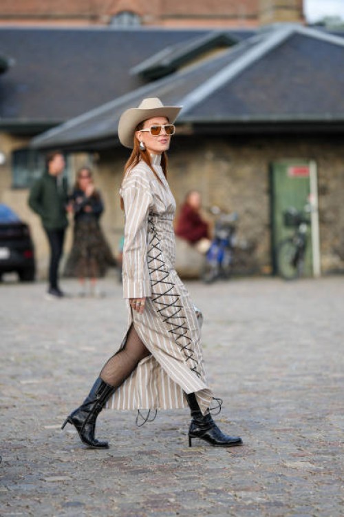 Guest wears a beige western hat, beige sunglasses, silver earrings, a beige and white striped print pattern shirt long dress with a black laces sides...