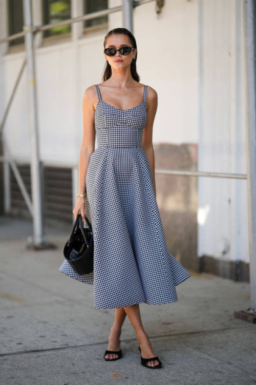 Guest wears a black and white checkered print pattern V-neck / tank-top / midi dress, a black shiny leather handbag, black suede heels mules, black...