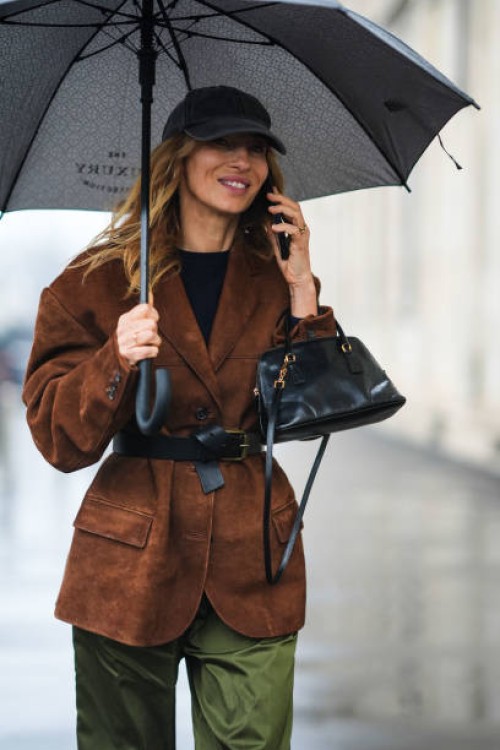Guest wears a black cap hat, a black top, a brown suede oversized blazer jacket, a black leather bag , outside Prada, during the Milan Fashion Week -...