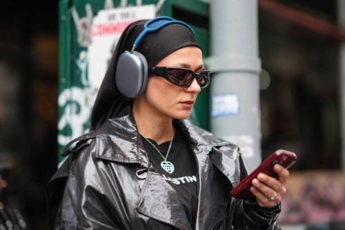 Guest wears a black headband, Apple airpods max, black sunglasses, a black and white t-shirt, a black leather jacket, outside La Pointe , during New...