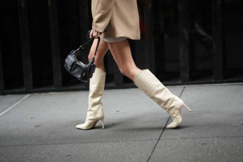 Guest wears a black leather bag, white pointed knee-high boots with high heels and crocodile pattern, outside Jason Wu, during New York Fashion Week,...