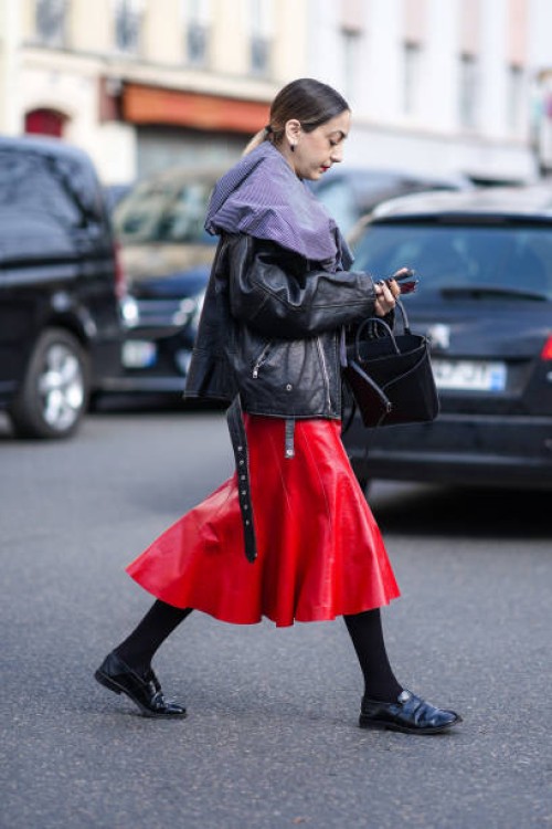 Guest wears a black leather jacket, a red leather midi skirt, tights, black leather shoes, a black leather bag, outside Undercover, during the...
