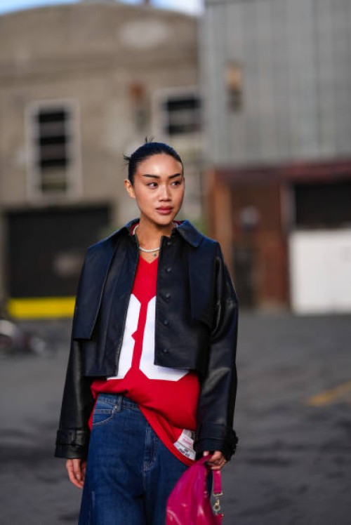 Guest wears a black leather jacket , red top, blue flared denim jeans pants , a red bag, outside Gestuz, during the Copenhagen Fashion Week AW24 on...