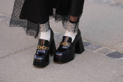 Guest wears a black polka dots print pattern tulle long skirt, white socks, black shiny varnished leather block heels / platform loafers, outside...