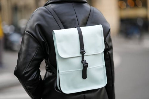 Guest wears a black shiny leather puffy / belted coat, a black and blue leather back pack bag, outside The Row, during Paris Fashion Week -...