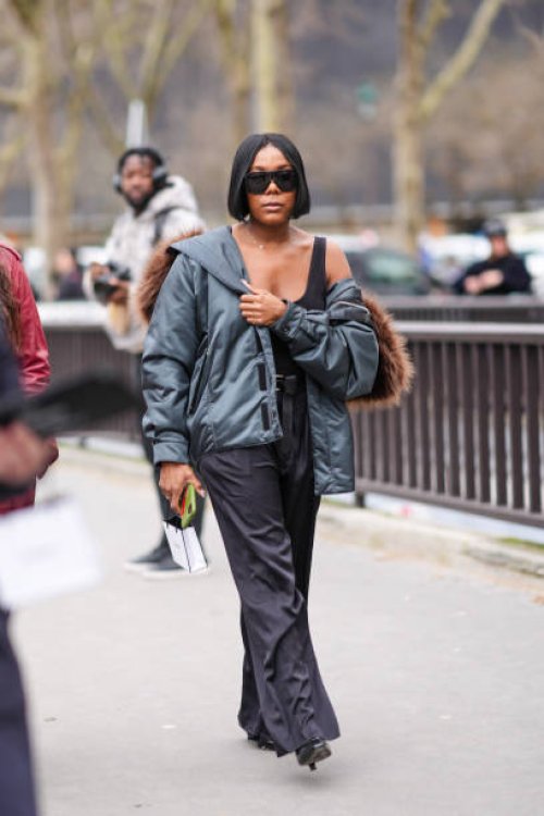 Guest wears a bomber jacket with brown fur, a black tank top, black wide-leg pants, black high heels, sunglasses, outside Chanel, during the...