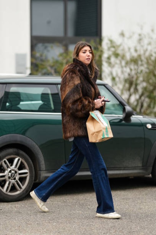 Guest wears a brown faux fur fluffy jacket, dark blue denim jeans : pants, white leather sneakers shoes, outside Jordanluca, during the Milan Fashion...
