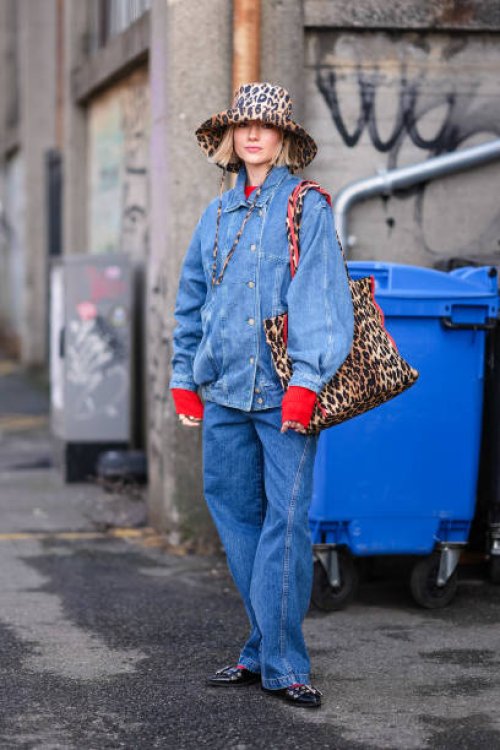 Guest wears a brown leopard print pattern hat, a matching tote bag, a blue denim jacket , blue flared denim jeans pants , a red pullover , pointed...