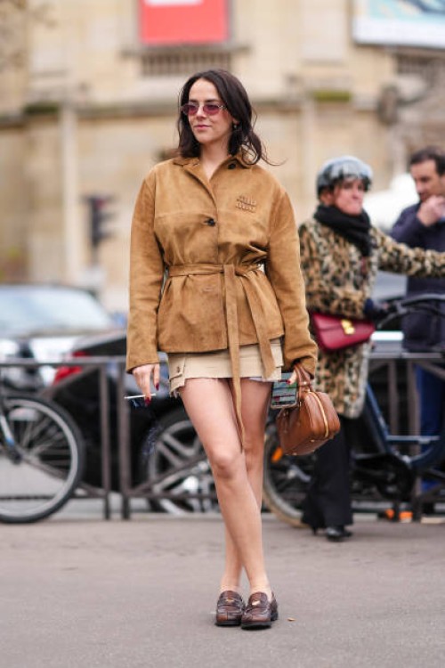Guest wears a brown suede jacket , a mini skirt , a leather bag, leather shoes, outside Miu Miu , during the Womenswear Fall/Winter 2024/2025 as part...