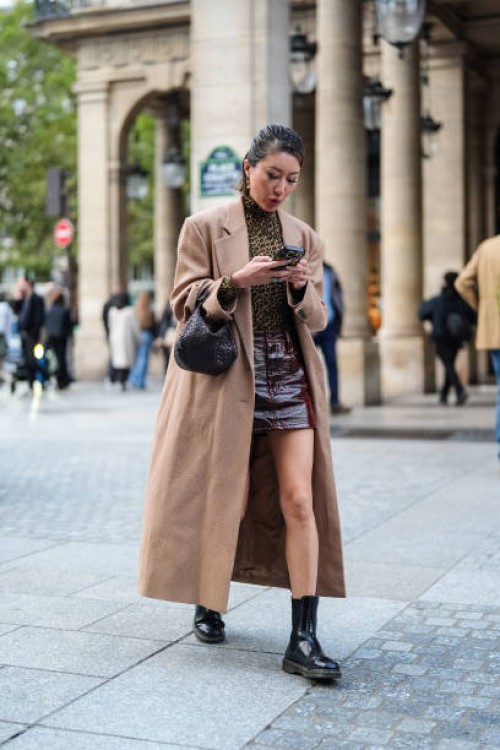 Guest wears a brown trench coat, a brown top with leopard patterns, a dark brown / burgundy leather skirt, a black leather bag, black leather boots,...