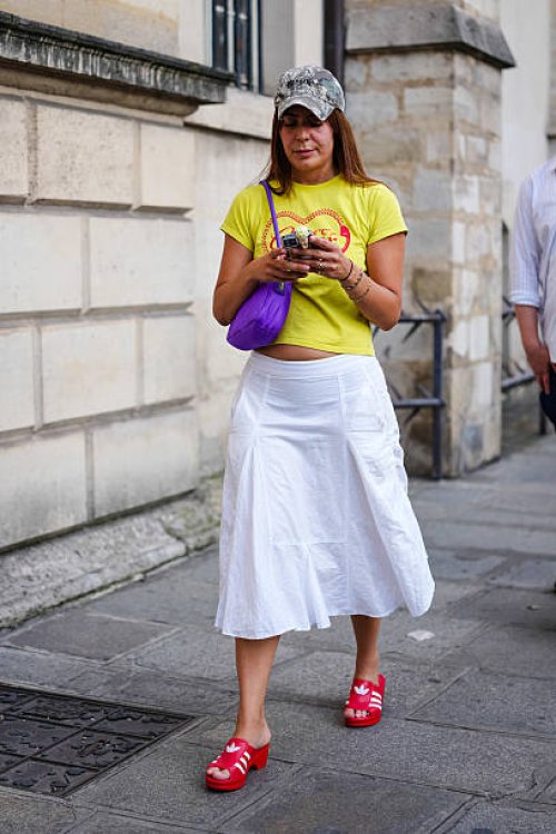 Guest wears a camouflage-patterned baseball cap and a bright yellow cropped T-shirt with a graphic print in red. A purple shoulder bag with a curved...