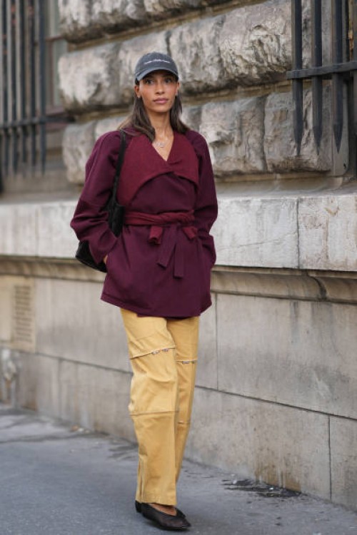 Guest wears a cap hat, a purple / burgundy wool coat, yellow trousers, mesh black shoes, outside Hermes, during the Womenswear Spring/Summer 2024 as...