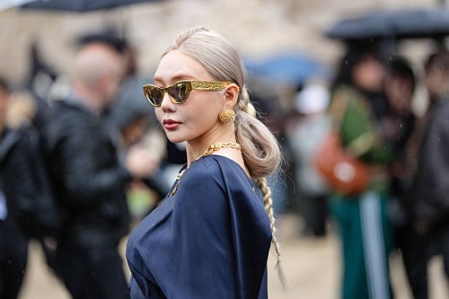 Guest wears a dark blue satin ensemble featuring a draped top with a cutout detail at the waist and long sleeves. The outfit includes a matching...