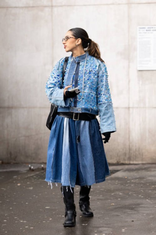 Guest wears a denim jacket embellished with blue rhinestones, a black leather belt, a denim round skirt, a black leather bag , black gloves and black...