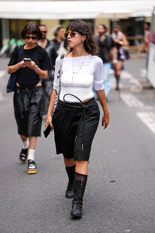 Guest wears a fitted white top with three-quarter sleeves. Sunglasses with a brown tint are worn, along with hoop earrings and a delicate chain...