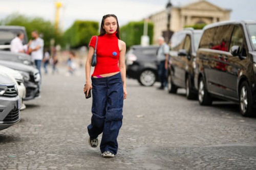 Guest wears a gold earring, a red fluffy / ribbed turtleneck short sleeves / asymmetric shoulder pullover with a blue embroidered pattern, a blue...