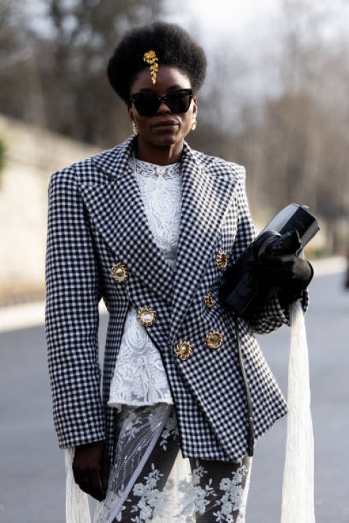 Guest wears a gold hair accessor, a white lace top, a black and white checked jacket with gold buttons, a black bag, black gloves and a white tulle...