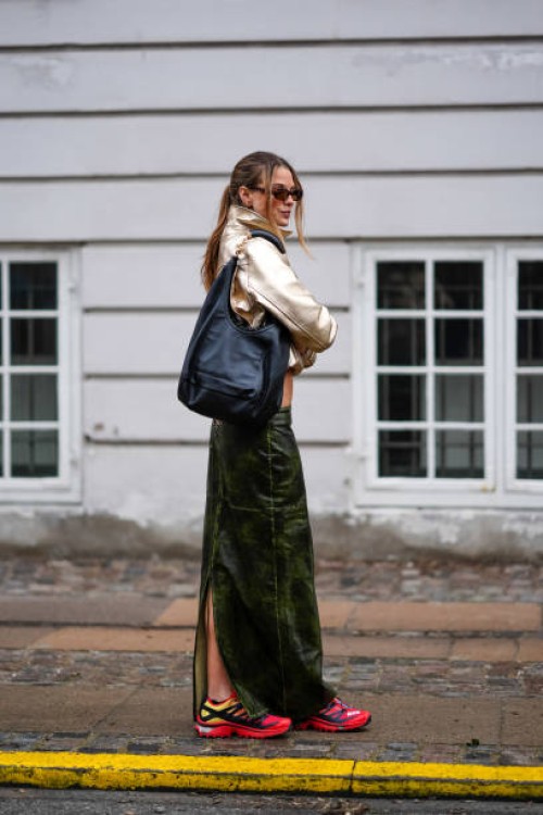 Guest wears a golden jacket, a green leather long skirt, red sneakers shoes, a black leather bag, outside Lovechild 1979, during the Copenhagen...