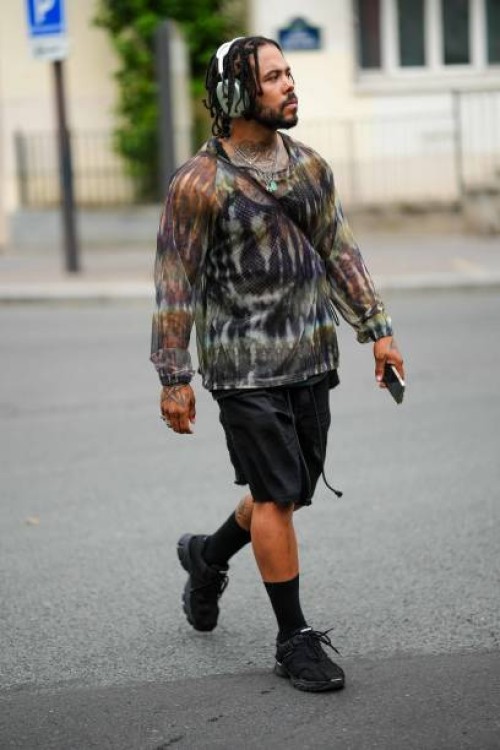 Guest wears a green headphones, a black mesh / fishnet tank-top, a brown / khaki / black tie and dye print pattern long sleeves t-shirt, black suit...