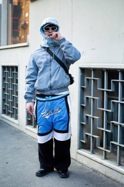 Guest wears a grey baclava, grey sunglasses, a black crossbody bag, a grey jacket, black, white and light blue wide leg trousers and black shoes...