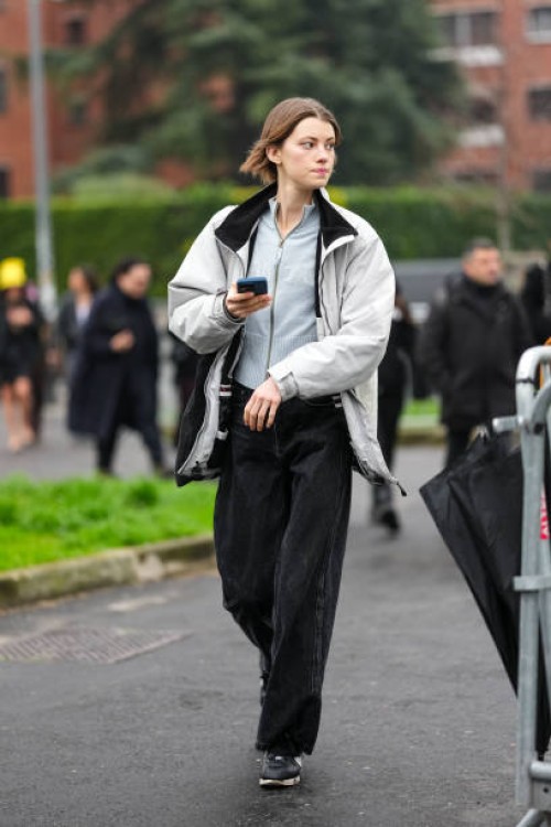 Guest wears a grey pullover, a white and black jacket, black wide-leg denim jeans / pants, black sneakers shoes, outside Gucci, during the Milan...