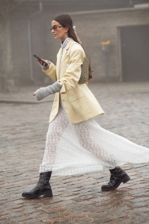 Guest wears a long white maxi skirt, grey hand warmers, Dior bag, and pale yellow jacket outside Rolf Ekroth during the Copenhagen Fashion Week AW24...