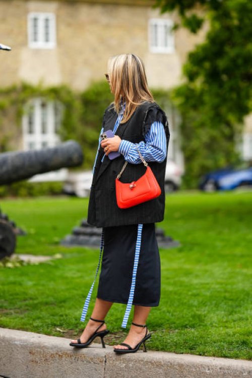 Guest wears a navy blue and white striped print pattern shirt, a black ripped denim sleeveless oversized jacket, a neon orange matte leather handbag...