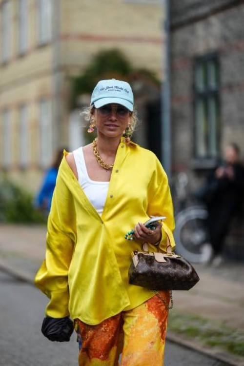 Guest wears a pale blue denim with embroidered navy blue inscriptions pattern cap, glasses, gold large pendant earrings, a gold large chain necklace,...