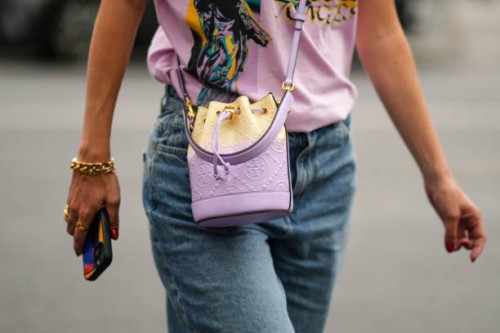Guest wears a pale purple with green and yellow print pattern t-shirt, a pale purple shiny leather embossed monogram pattern crossbody bag from Tory...