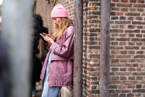 Guest wears a pink wool beanie hat, a purple leather jacket , blue denim jeans pants , outside The Garment, during the Copenhagen Fashion Week AW24...