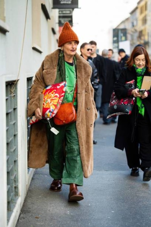 Guest wears a printed pillow as an accessor, an orange knitted hat, a beige teddy long coat, an orange leather crossbody bag, a green velvet blazer,...
