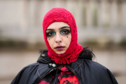Guest wears a red embossed pattern hoodie, a black oversized nylon zipper bomber coat, a black and red print pattern long sleeves / legging jumpsuit,...