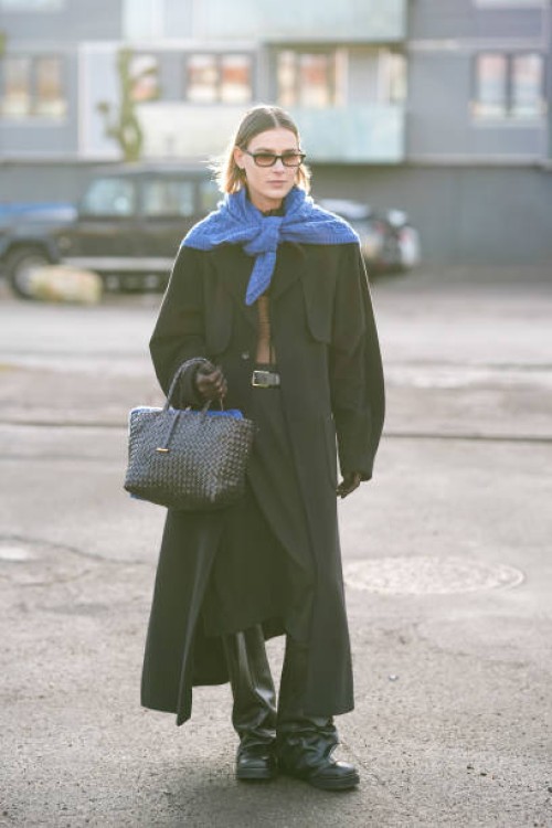 Guest wears a royal blue wool pullover worn as a scarf, a black long coat , a woven leather bag, outside The Garment, during the Copenhagen Fashion...