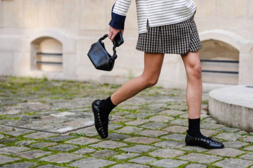 Guest wears a shiny black Ganni leather bag, black socks, shiny black laced flats leather shoes, outside Ganni, during the Paris Fashion week Women's...