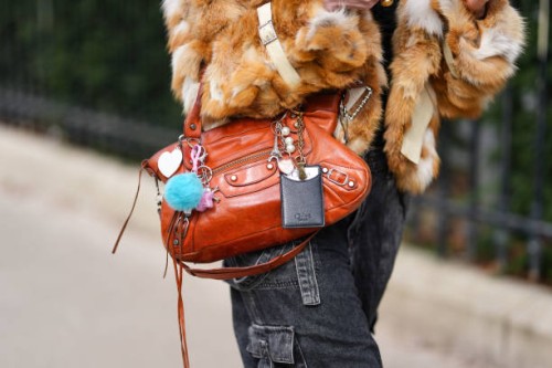Guest wears a shiny dark brown leather bag, bag charms, outside Lacoste, during the Paris Fashion week Women's Fall/Winter 2025-2026 on March 9, 2025...