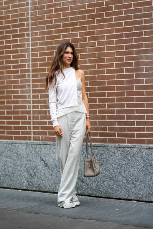 Guest wears a white cardigan, a white lace strappy lingerie top, white long pants, a light brown ba, outside Fendi, during the Milan Fashion Week -...