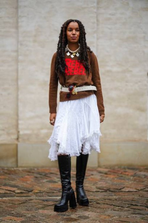 Guest wears a white large pearls with silver pendants necklace, a dark brown with embroidered red pattern pullover, a white latte matte leather belt,...