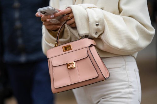 Guest wears a white latte ribbed velvet zipper jacket, a pale pink matte leather handbag from Fendi, white denim pants, gold necklaces, outside...