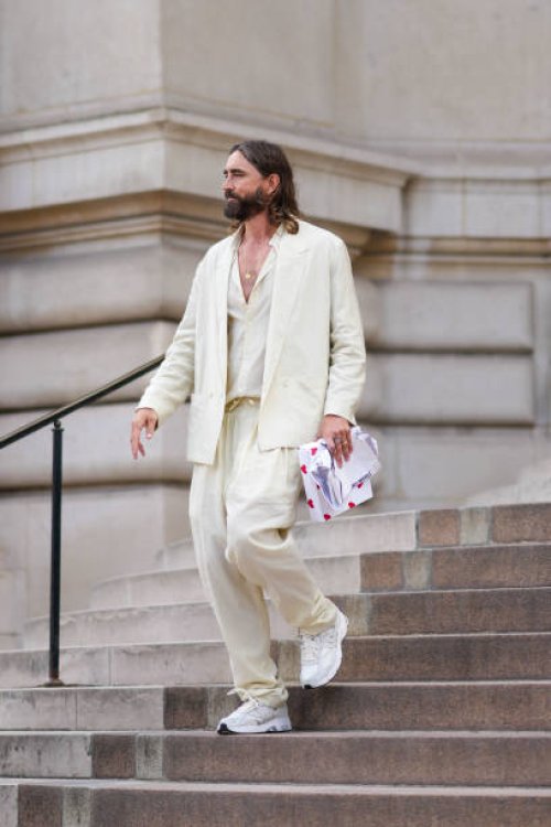 Guest wears a white latte V-neck shirt, a white latte blazer jacket, matching white latte suit large pants, a gold ring, white leather and fabric...