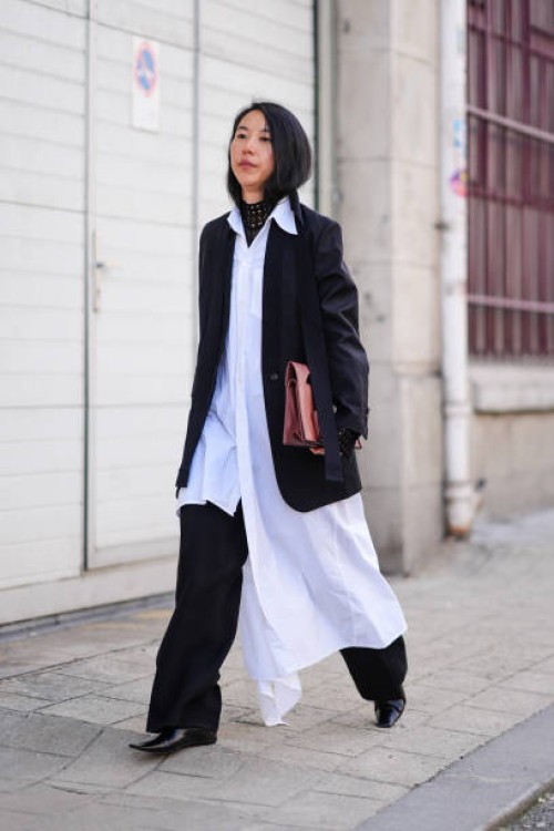 Guest wears a white long shirt / dress , black wide-leg pants, leather pointed shoes , a black oversized blazer jacket , outside Marine Serre, during...