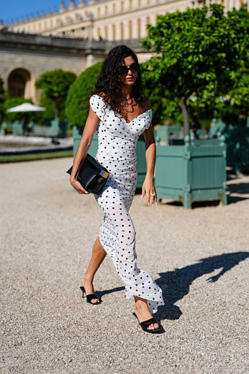 Guest wears a white off-the-shoulder dress with black polka dots, featuring a ruched design and a fitted silhouette. The dress extends to a midi...