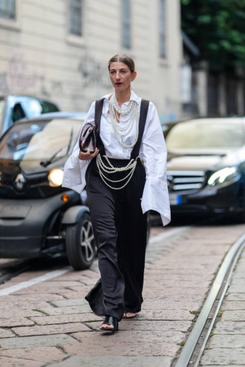 Guest wears a white oversized shirt, black overalls, pearl necklaces, dark brown leather bag, pearl necklaces as belt, black open-toe leather shoes,...
