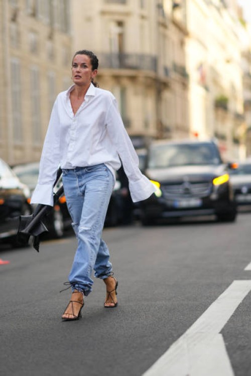 Guest wears a white oversized shirt, pale blue faded denim large pants, a black shiny leather chair from Alaia, black shiny leather strappy heels...