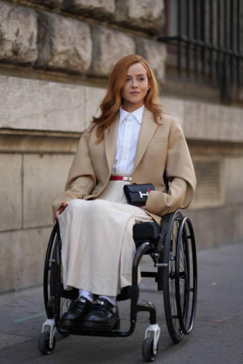 Guest wears a white shirt, a beige oversized blazer jacket, a belt, pleated skirt, a black mini Hermes bag, outside Hermes, during the Womenswear...