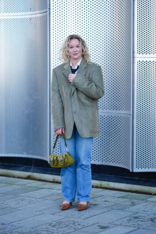 Guest wears a white shirt, black tie, a corduroy blazer jacket , a khaki green leather bag, blue denim jeans pants , brown pointed shoes, outside...