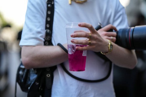 Guest wears a white t-shirt, a black shiny leather nailed / studded Cagole shoulder bag from Balenciaga, a gold watch, gold rings, gold Love rings...