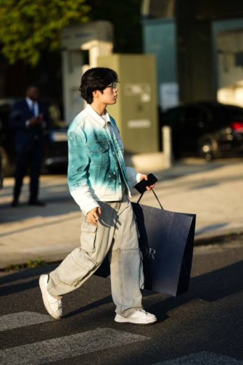Guest wears a white t-shirt, a white and green tie and dye print pattern denim jacket, pale blue faded denim large cargo pants, a black shopping bag...